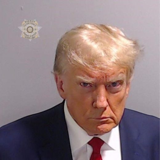 Vêtu d'un costume marine et d'une cravate rouge impeccablement nouée, Donald Trump fixe l'objectif avec une mine renfrognée, front plissé et mâchoire serrée pour sa photo d'identité judiciaire..